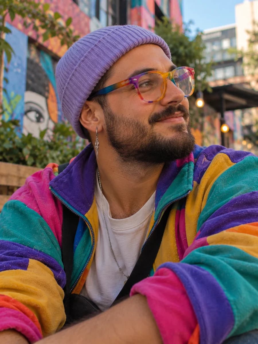 Man with a purple beanie and colourful glasses in a street with murals